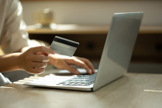 Close up of woman holding a credit card and typing on laptop, internet banking, or secure digital purchases..
