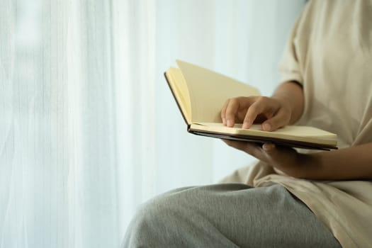 Peaceful young woman holding an open notebook sitting by a softly lit window.