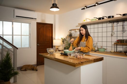 Happy asian woman in apron preparing meal in a stylish home kitchen.