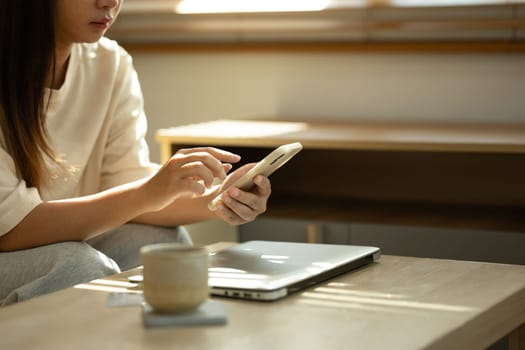 Young woman sitting in a cozy living room and using mobile phone.