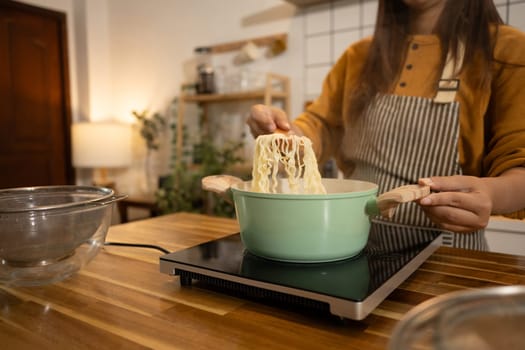 Close up woman lifts cooked noodles from a green pot on an induction stove.