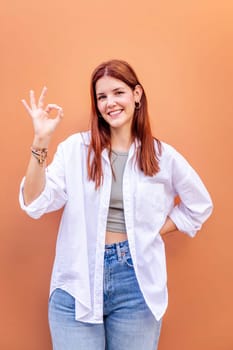 young woman doing ok sign with hand while smiling looking at camera in a positive and friendly mood suggesting that she is happy and content, copyspace for text