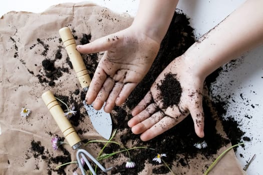 Child hands gardening with soil and flowers on brown paper.