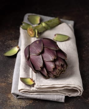 Head of purple raw romanesco artichoke on dark table closeup. Fresh vegetables bought on farmers market ready to cook on linen napkin. Italian cousine ingredient