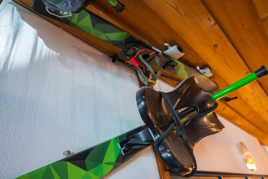 Green and black skis with geometric patterns, ski poles, and a black ski boot mounted on wooden paneling under warm lighting in a luxury hotel.