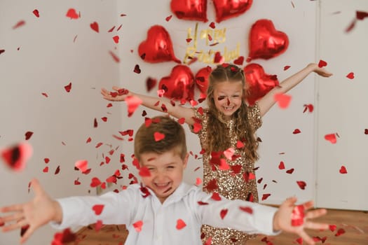 Children enjoy heart-shaped confetti. Balloons are in the background.Valentines Day concept