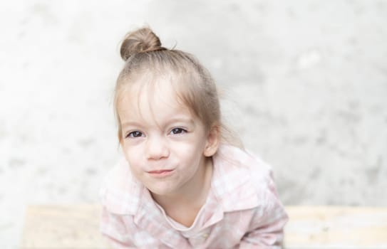 Close-up portrait of a young girl on a light background, gazing directly into the camera. Her innocent expression and soft natural light create a gentle and heartfelt moment