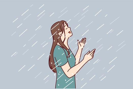 Woman enjoys rain standing under drops falling from sky in wet t-shirt and raising head up. Happy young girl rejoices in autumn rain after long summer drought caused by hot climate