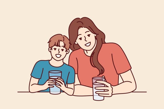 Happy mom and son drink water from transparent glasses and smile enjoying clean refreshing beverage. Positive family with water look at camera together and smile urging to drink more liquid