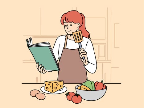 Woman with cookbook is standing in kitchen wanting to cook delicious dinner and vegetables and cheese with eggs. Girl cook in apron uses cookbook while preparing salad or appetizers