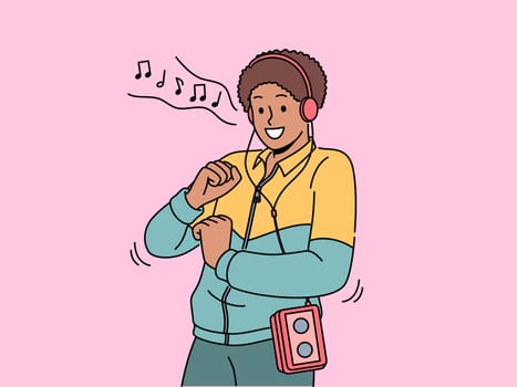 African American man in retro clothes with cassette player on belt listens to music in old-fashioned headphones. Ethnic hippie guy from 90s dances to reggae music playing in tape recorder