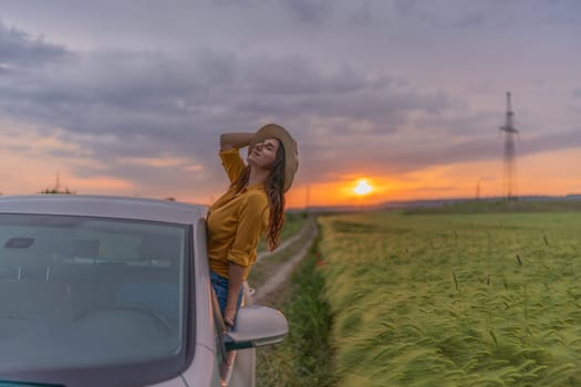 A woman in a yellow shirt is leaning out of a car window and looking up at the sun