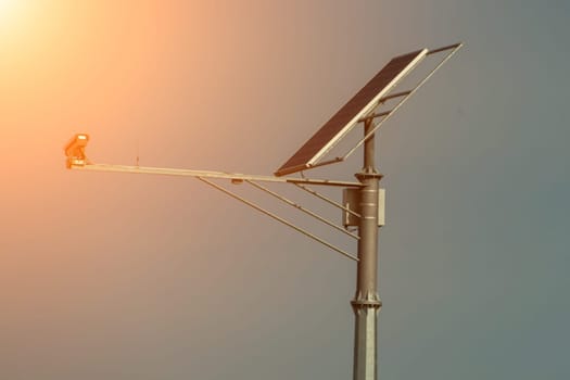 Solar-powered streetlight with a small bird perched on the arm, angled towards a setting sun. The light is attached to a tall pole against a muted sky.