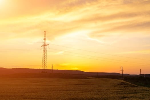 Sunset silhouettes two communication towers standing tall over a golden field and rolling hills. Warm, hazy light bathes the landscape.