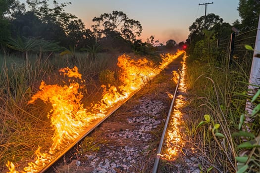 Dramatic evening scene of flames along railway track during sunset.