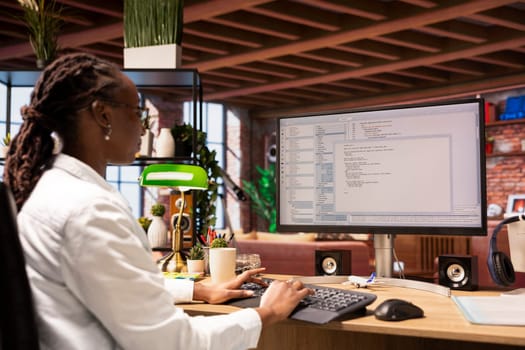 Woman in home office looking at UI on computer screen, typing and executing programming code. Coding application UI used by african american IT developer writing and testing code in modern apartment