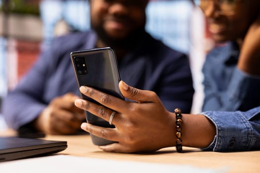 Home office freelancer attending online video call from their house, using smartphone app to join colleagues at a webinar. African american remote workers together at desk, teleconference.