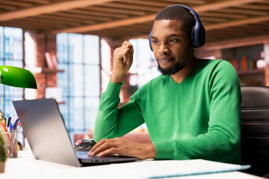 Remote employee wearing headphones at home participating in online training session on laptop. Teleworker using audio device at home to watch instructional course videos on notebook