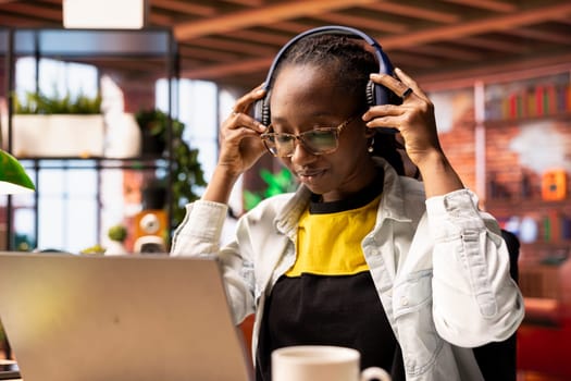 Smiling woman in modern apartment wearing headphones, listening music during relaxation time, feeling pleased. Person having fun at home hearing exciting songs through audio headset device
