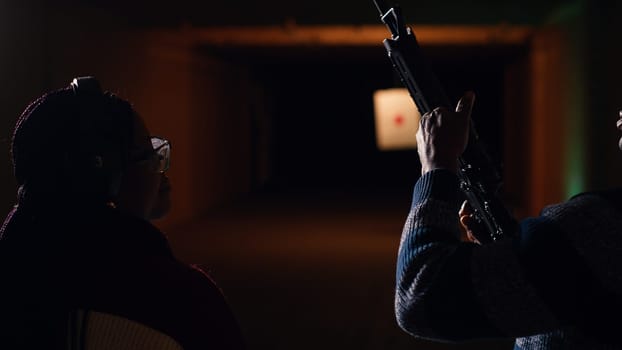 Man holds rifle, enjoying recreational shooting experience in firing range next to group of friends. People practicing with weapons in safe environment at shooting range company, camera B