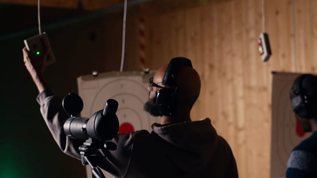 Firing range client doing shooting activity next to friends, zooming to check if he shot bullseye. Person analyzing targets shot using magnifying lens, comparing results with mates, camera B