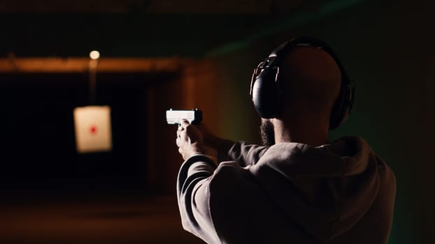 Person wearing protecting gear loading magazine in pistol during firearm practice session at shooting range. Gun enthusiast reloading handgun, learning self defense, pointing weapon, camera B