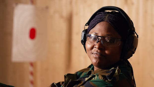Smiling woman in firing range doing recreational shooting activity with firearm, hitting bullseyes. Happy person in shooting gallery training with handgun, developing muscle memory, camera B