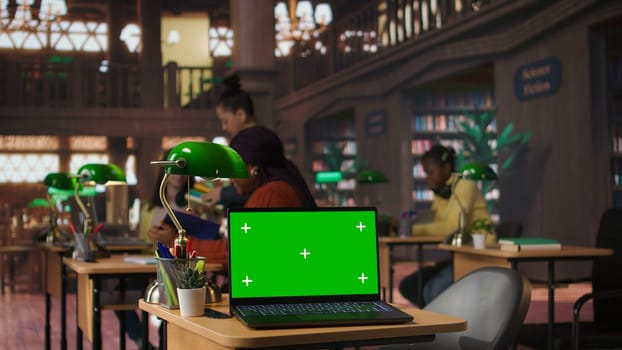 Diverse schoolgirls work with professors on homework next to mockup screen, focused on writing an essay in a school library. Scholars completing their assignment on textbooks. Camera A.