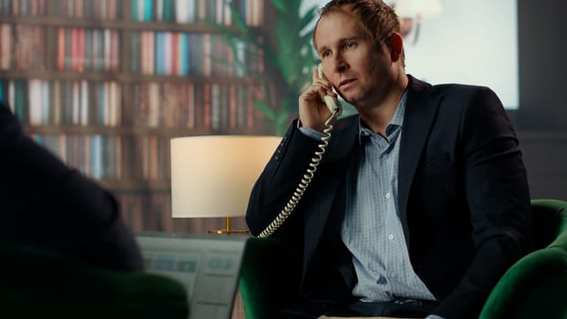 Intelligence officer on a secure line answering phone call in CIA safe house, gathering field information from undercover informants scattered around the city. Sensitive details. Camera B.