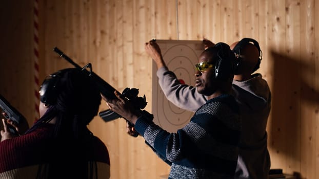 Group of friends in firing range shooting targets, wearing earmuffs to protect hearing. People reloading weapons, using safety gear to prevent damage from gunshots, camera B