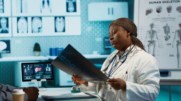 General practitioner reviewing x ray imaging at checkup with male patient, offering her professional expertise to ensure wellness. Medic doing scan interpretation with a man in the office. Camera A.