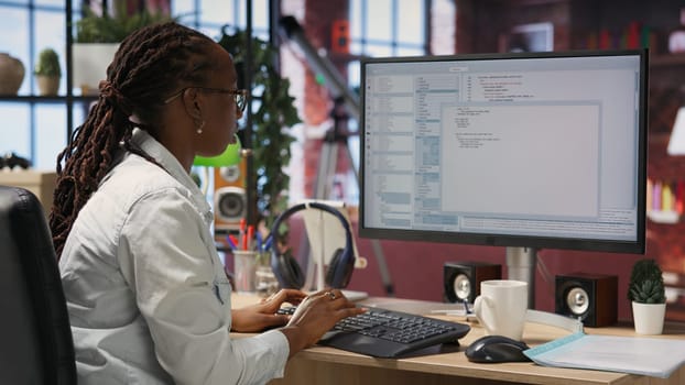 Engineer in home office looks at UI on computer monitor, typing and executing programming code. Panning shot of IT worker using coding application to write and test code in modern apartment, camera B