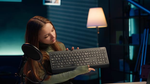 Entertainer presents keyboard and mouse from brand sponsoring video, urging viewers to buy it. Young girl does influencer marketing by advertising computer peripherals to audience in studio, camera A