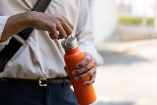 A man is seen opening his orange reusable water bottle, showcasing sustainable hydration choices while minimizing plastic waste.