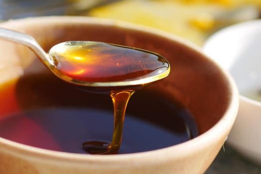 Golden honey flows from a spoon into a clay bowl on a sunny day.
