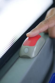 A hand gently presses the stop button inside a bus.