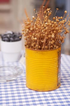Dried flowers are arranged in a yellow tin on a checkered table.