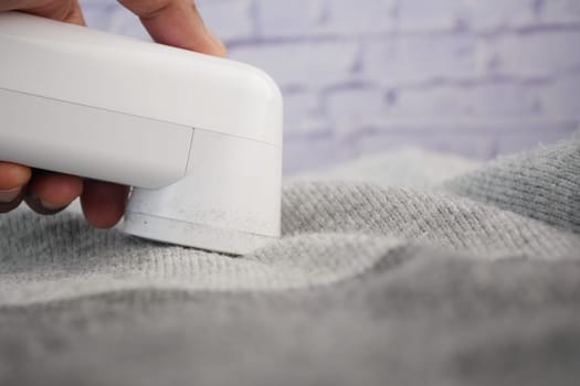 Person using a lint remover on grey fabric to clean it from lint.