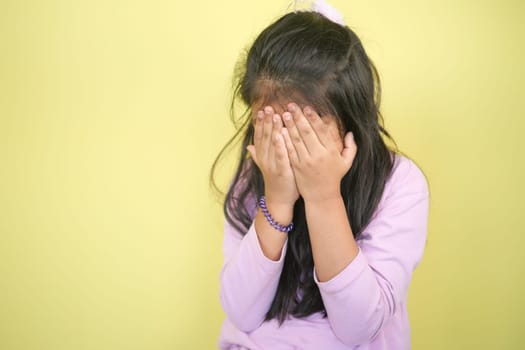 A young girl hides her face with hands, expressing emotions inwardly.