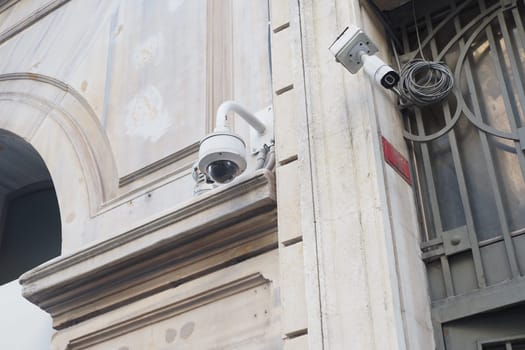 Two security cameras are positioned on a building corner with a textured wall.