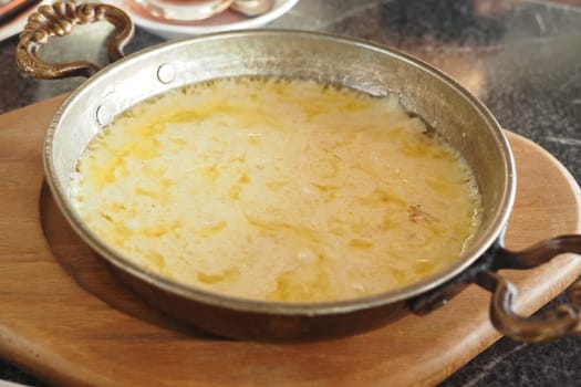 Savory melted cheese served warm in a rustic pan on a wooden board.