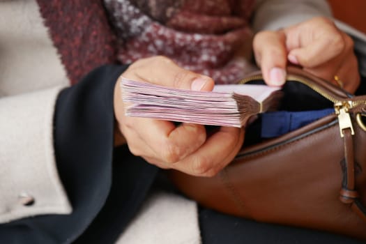 A woman is holding a thick stack of cash while sitting quietly.