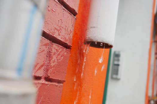 Water cascades from a rain gutter against a vibrant wall.
