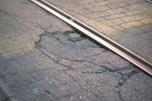 Cracked pavement next to railway tracks during evening light.