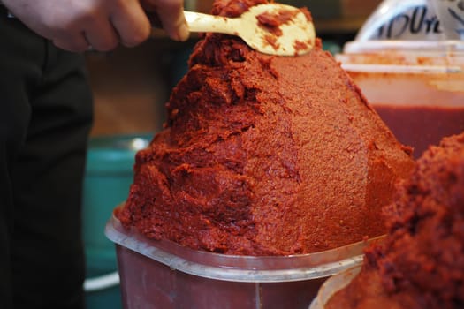 A vendor prepares vibrant red pepper paste in a bustling market.