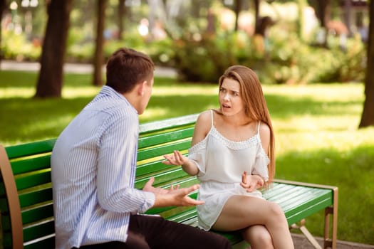 Relationship problems concept. Millennial couple having argument on bench at summer park