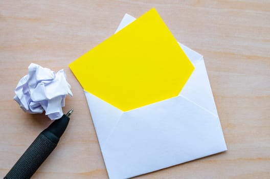 Top view of empty yellow notepad inside an envelope with crumpled paper and pen with customizable space for text.