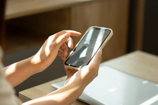 Young woman using mobile phone at coffee table with soft sunlight streaming through the window.