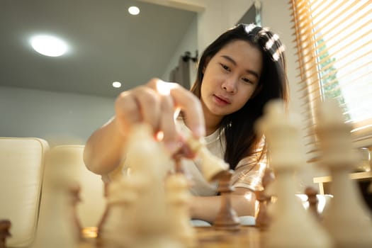 Young asian woman enjoying a game of chess, moving a piece on wooden board.