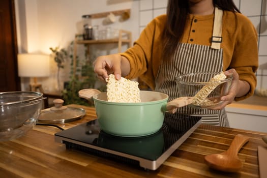 Close up shot of woman putting dried instant noodles into a boiling pot.